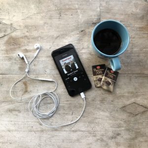 Image of a mobile phone with headphones attached, tuned into a podcast, next to a coffee mug.